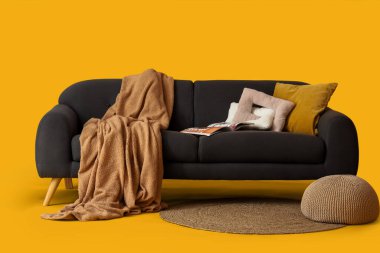 Yastıkları, battaniyesi, dergisi ve sarı arka planı olan rahat siyah kanepe.