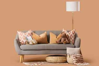 Yastıklı rahat gri kanepe, hasır tepsi, sepet ve zemin lambası kahverengi arka planda