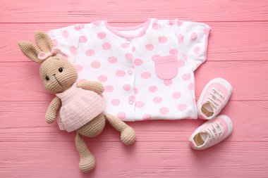 Bebek kıyafeti, oyuncak tavşan ve pembe tahta arka planda popolar.