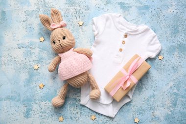 Örgü oyuncak tavşan, bebek tulumu ve renk arka planında hediye kutusu olan kompozisyon