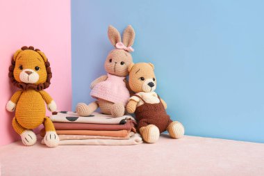 Bebek kıyafetleri yığını ve renkli arka planda sevimli örülmüş oyuncaklar.