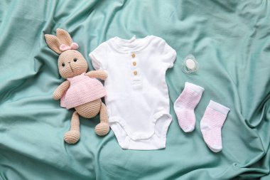 Bebek kıyafetleri, emzik ve oyuncak tavşan renkli kumaş arka planda