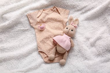Oyuncak tavşan, bebek tulumu ve hafif kumaş arka planda emzik.