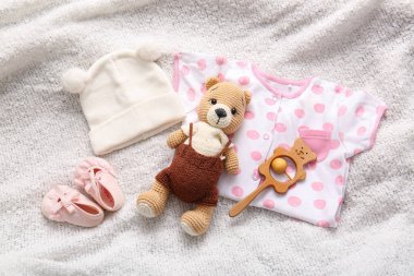 Bebek kıyafetleri, patik ve oyuncak kompozisyonu açık kumaş arka planda
