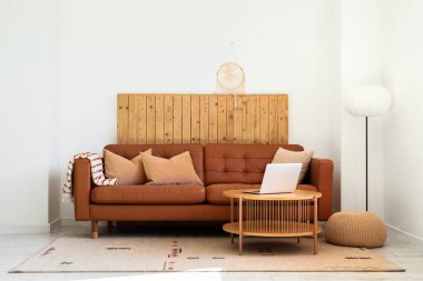 Oturma odasının içinde lamba, şık deri kanepe ve beyaz duvarın yanındaki sehpada dizüstü bilgisayar.