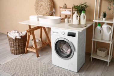 Modern çamaşır makinesi, lavabo ve deterjan şişeleriyle şık bir çamaşır odası.