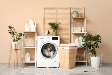 Modern çamaşır makinesi, sepet, raf ünitesi ve deterjan şişeleriyle şık bir çamaşır odası.