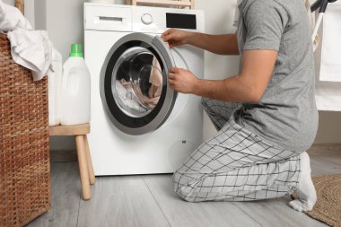 Çamaşır odasındaki modern çamaşır makinesine çamaşır koyan genç adam.