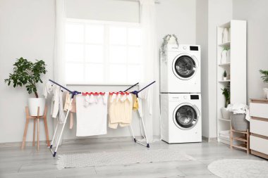 Modern çamaşır makineleri, kurutma rafları ve deterjan şişeleriyle şık bir çamaşır odası.