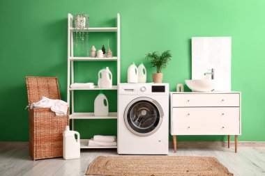 Modern çamaşır makinesi, hasır sepeti, lavabosu ve deterjanı olan şık bir çamaşır odası.