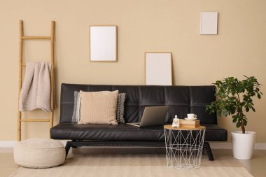 Modern siyah kanepesi, dizüstü bilgisayarı, kahve masası ve puf olan şık bir oturma odası.