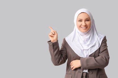 Türbanlı güzel Müslüman kadın gri arka plandaki bir şeyi işaret ediyor.