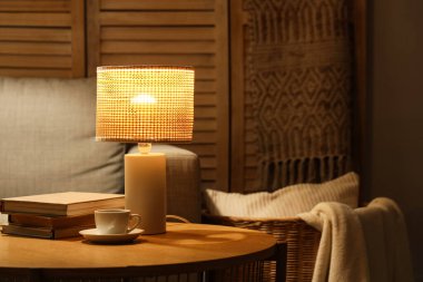 Geceleri oturma odasındaki masada kitap ve kahveyle parlayan lamba.