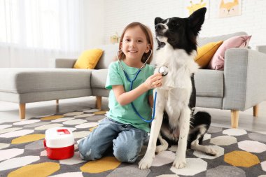 Steteskoplu şirin küçük kız evde halıda köpek dinliyor.