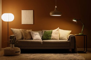 Konforlu kanepesi olan modern bir oturma odası, puf ve parlayan lambaları olan bir çiçek.