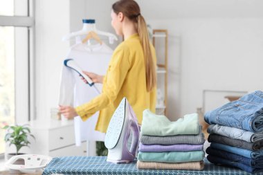 Odasında bir yığın temiz giysi, demir ve kadın olan ütü masası.