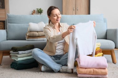 Güzel genç bir kadın evde yerde otururken temiz giysileri istifliyor.