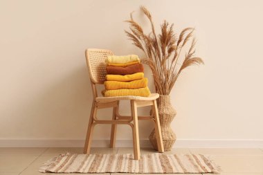 Şık bir sandalyede ve vazoda bol bol kalın elbiseler ve renkli duvarların yanında otlar.