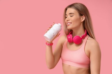 Kulaklıklı, pembe arka planda su içen genç bir bayan.