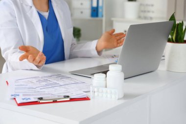 Dizüstü bilgisayarı olan kadın doktor ofis masasında sohbet ediyor, yakın plan.
