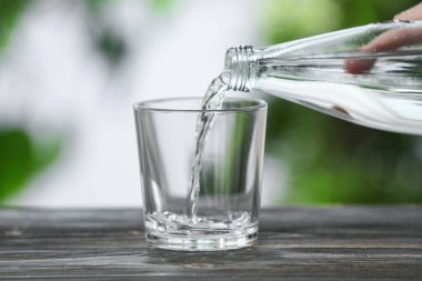 Kadın şişeden bardağa temiz su dolduruyor.