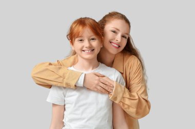 Genç kızıl kadın ve tatlı kızı gri arka planda sarılıyorlar.