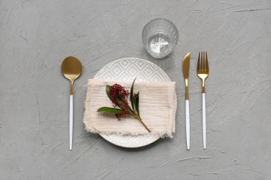 Altın çatal bıçak takımı ve gri arka planda skimmia japonica bitkisi olan güzel bir masa.