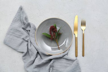 Altın çatal bıçak takımı ve gri arka planda skimmia japonica bitkisi olan güzel bir masa.