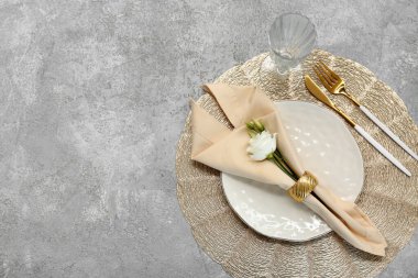 Altın çatal bıçak takımı ve gri arka planda östoma çiçekleri olan güzel bir masa.