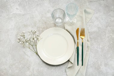 Altın çatal bıçak takımı ve gri arka planda çigila çiçekleri olan güzel bir masa.