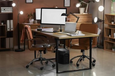 Boş bilgisayar monitörü, dizüstü bilgisayarı ve parlak lambası olan bir işyeri.