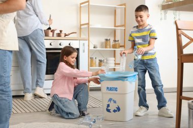 Çocuklar çöp kutusuna plastik çöp atıyor ve aileleri de mutfakta. Küresel Geri Dönüşüm Günü