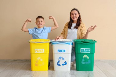 Anne ve oğlu bej duvarın yanında çöp konteynırları taşıyorlar. Küresel Geri Dönüşüm Günü