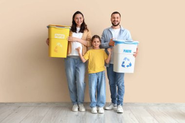 Bej duvarın yanında çöp bidonları olan bir aile. Küresel Geri Dönüşüm Günü