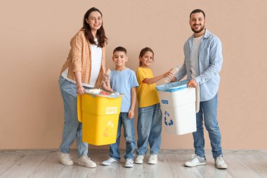 Bej duvarın yakınındaki çöpleri ayıran konteynırları olan bir aile. Küresel Geri Dönüşüm Günü