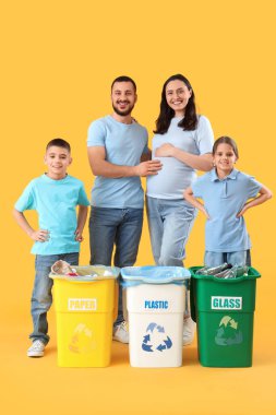 Sarı arka planda çöp bidonları olan bir aile. Küresel Geri Dönüşüm Günü