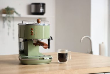 Mutfaktaki masada cam bir bardak espresso ile kahve makinesi.