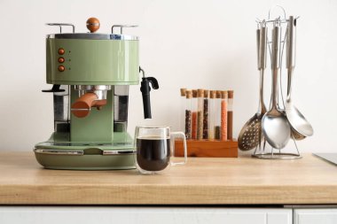 Mutfaktaki masada cam bir bardak espresso ile kahve makinesi.