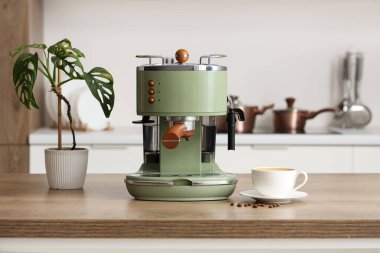 Kahve makinesi ve bir fincan espresso ve mutfak masasında bitki.