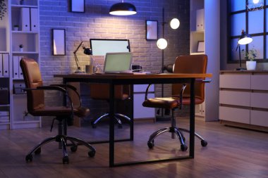 Boş dizüstü bilgisayarı olan bir işyeri ve geceleri karanlık ofiste parlayan lambalar.