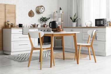 Mutfağın içinde elektrikli çaydanlık, lezzetli haşhaşlı çörekler ve masanda fincanlar.