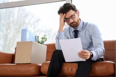 Görevden alındığı için üzgün genç bir adam koltukta oturuyor.