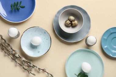 Different clean plates with Easter eggs with fresh leaves and pussy willow branches on light background
