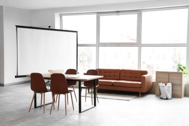 Konferans salonunun içinde projektör ekran, kanepe ve masa var.