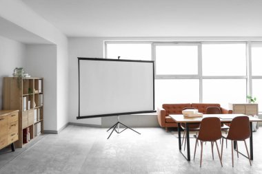 Konferans salonunun içinde projektör ekran, kanepe ve masa var.