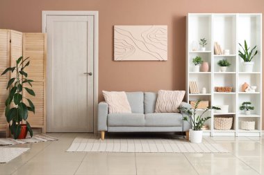 Konforlu kanepe, ev bitkisi ve oturma odasının içindeki raf ünitesi.