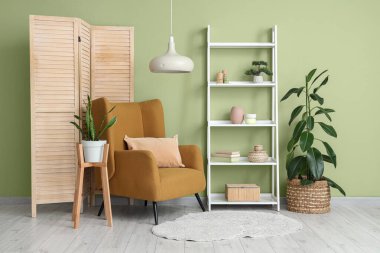 Koltuk, raf ünitesi ve yeşil duvarın yanındaki katlanan ekran.