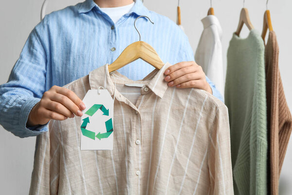Woman holding hanger with shirt and recycling tag on white background