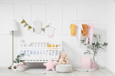 Bebek odasının içinde beşik, lamba ve bebek kıyafetleri var.