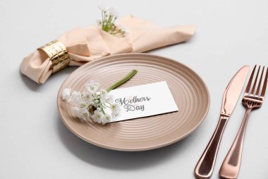 Tebrik kartı ve gri arka planda güzel çiçeklerle süslü masa ayarları, yakın plan. Anneler Günü kutlaması